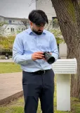 Arda Sözeri im hellblauen Hemd prüft die Aufnahme an seiner Kamera in einem Park